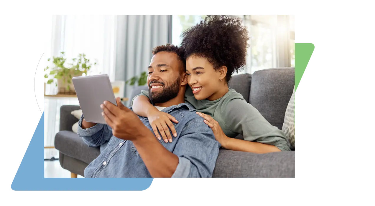 A young couple smiling and lounging on a sofa using a tablet